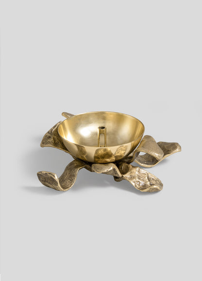 The Glory Lily Eternal Diya by VIYA features a gold bowl with a central handle, gracefully perched atop a sculptural, abstract gold base inspired by organic, wavy leaves—all set against a plain light gray background. This captivating design harmoniously blends ancient metalworking artistry with the timeless allure of a modern heirloom.