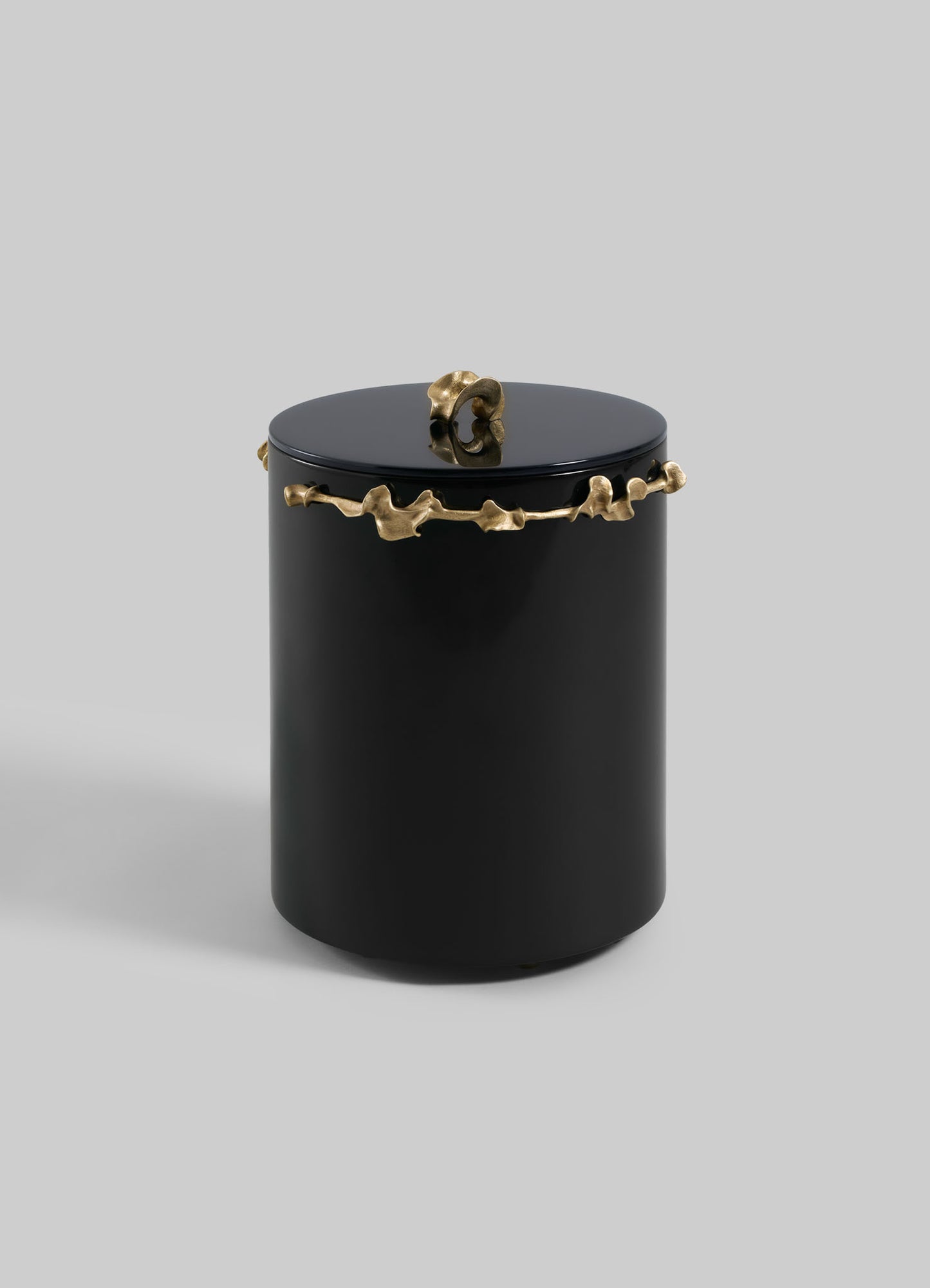The VIYA Saffron Black Bin With Lid is a sleek, cylindrical black container with a matching lid, adorned with an abstract gold saffron-inspired design around the top and a small gold accent on the lid, set against a plain light gray background.