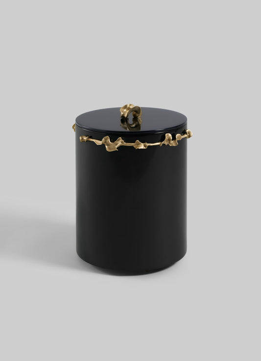 The VIYA Saffron Black Bin With Lid is a sleek, cylindrical black container with a matching lid, adorned with an abstract gold saffron-inspired design around the top and a small gold accent on the lid, set against a plain light gray background.