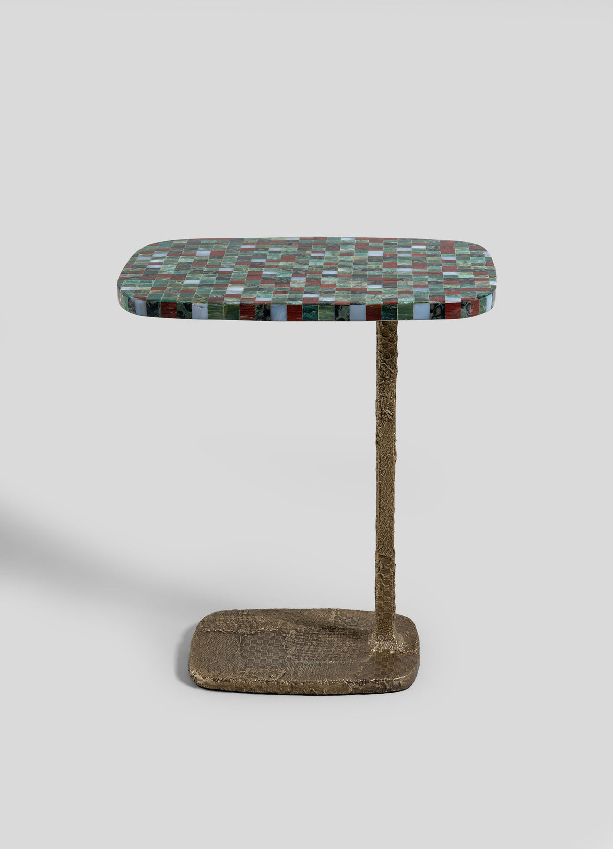 The VIYA Mosaic Red Side Table features a compact, rectangular top adorned with a multicolored mosaic-inspired checkered design, supported by a single textured bronze stem and a cast brass base, shown against a simple light gray backdrop.