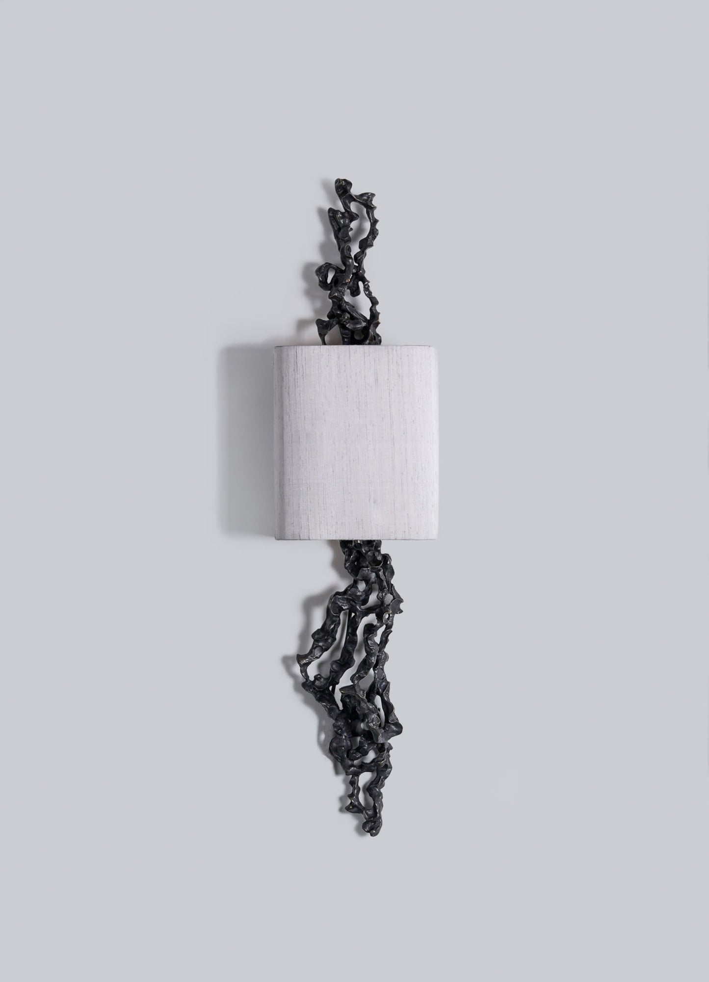 The Andaman Wall Sconce A by VIYA features a rectangular, light block with textured black organic forms projecting from the top and bottom, set against a plain light gray background.