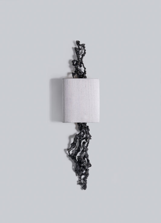 The Andaman Wall Sconce A by VIYA features a rectangular, light block with textured black organic forms projecting from the top and bottom, set against a plain light gray background.