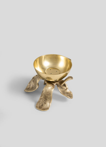 The Glory Lily Incense Diya by VIYA features a gold bowl with a smooth finish, poised atop an abstract, organic-shaped base textured like roots or coral. Its intricate design subtly echoes ancient metalworking techniques, creating a modern heirloom that seamlessly blends artistry and heritage—set against a plain gray background.