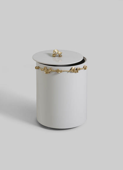 The VIYA Saffron Ecru Bin With Lid is a white cylindrical container with gold accents and vine-like gold details, evoking bronzed decor. The lid sits slightly ajar against a light gray background.