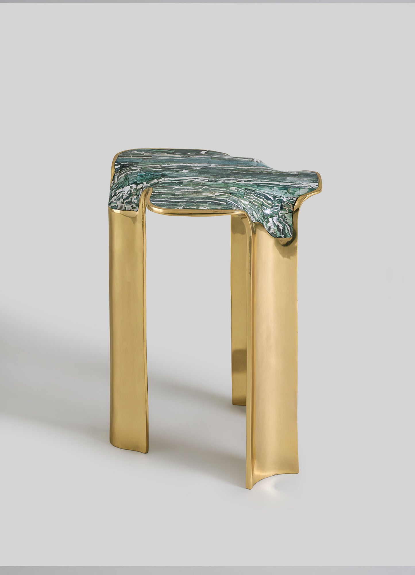 The VIYA Coonoor Side Table features a sculptural design with three gold legs and an irregular, textured turquoise-green top inspired by Indian landscapes, set against a plain light gray background.