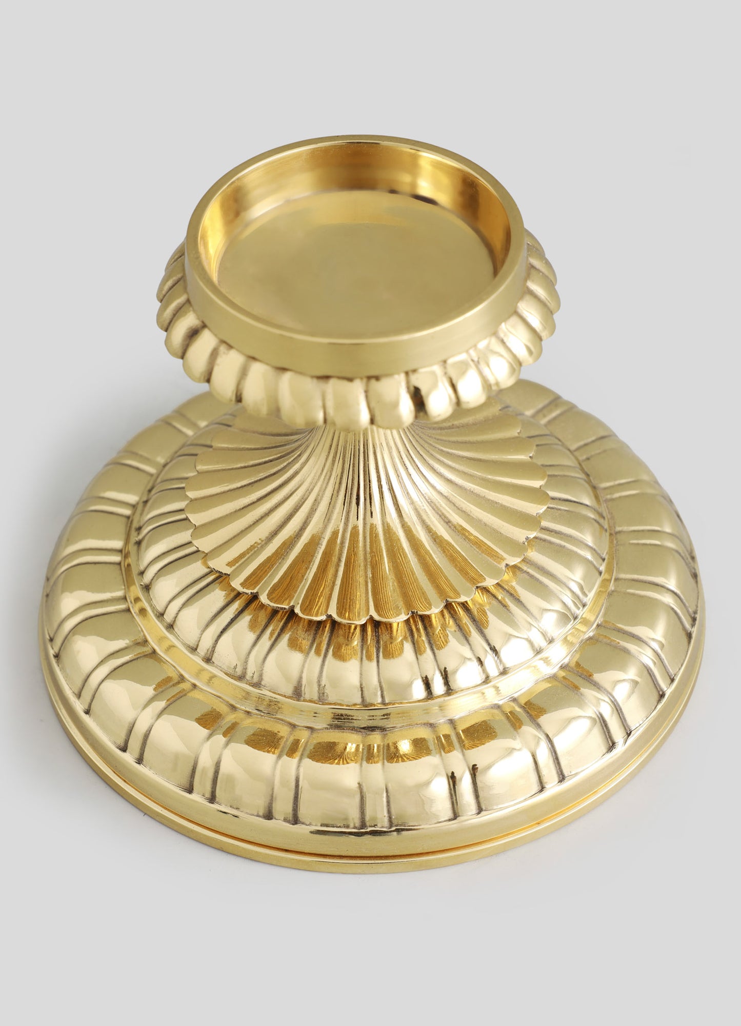 Decorative gold-colored candle holder with a scalloped and ribbed design, featuring a rounded base and a wide, flat top for candles. Made of metal with a shiny finish, combining classic motifs with a luxurious style.