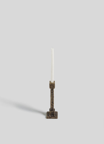 The VIYA Tiruppur Candle Holder Small, with an antique-style bronze finish reminiscent of Indian brocades, holds a single white candle upright against a plain light gray background. The candle’s soft shadow falls to the left.