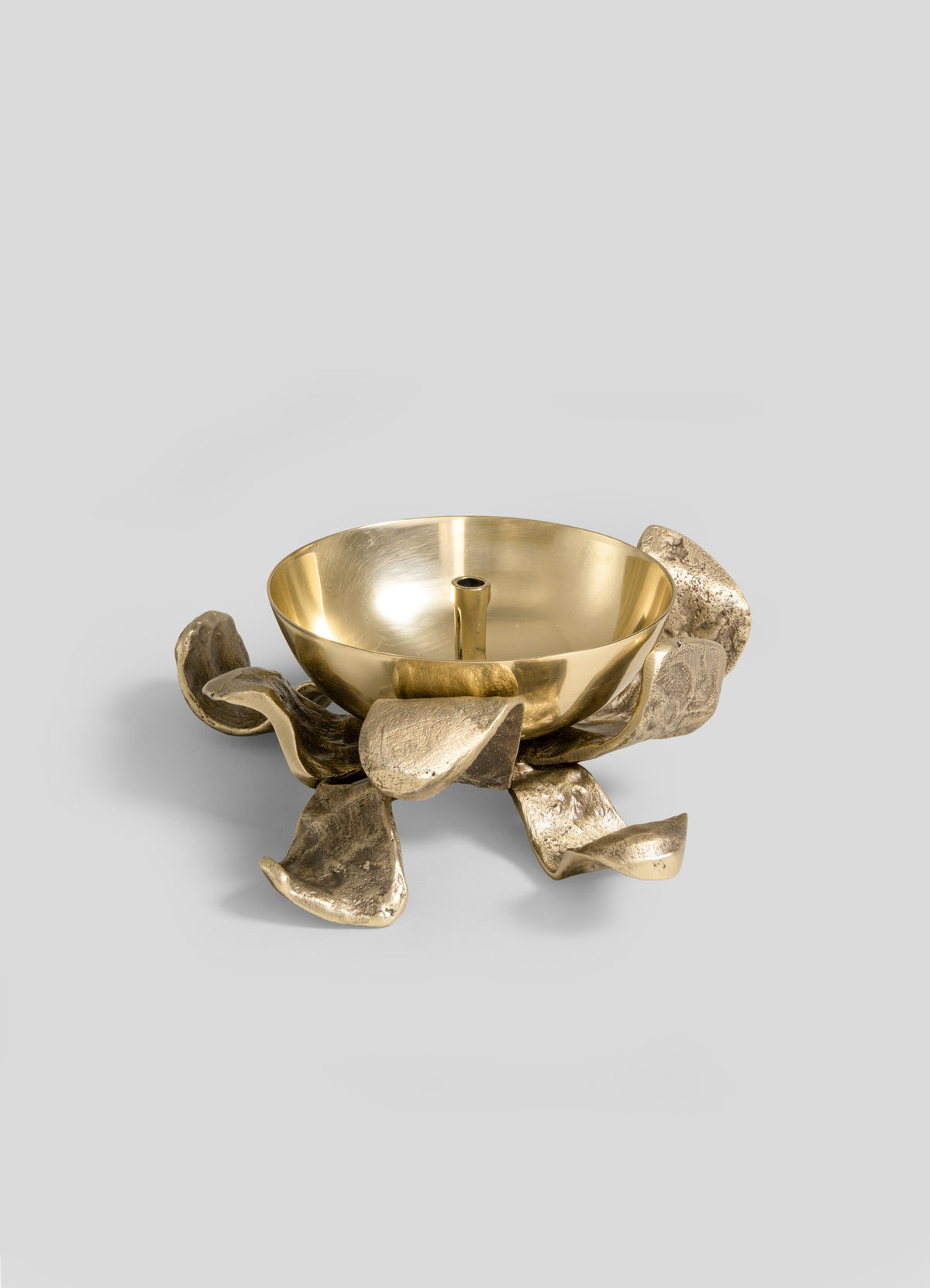 The VIYA Glory Lily Eternal Diya features a shiny gold bowl with a central handle, elegantly perched on an ornate, textured base reminiscent of wavy abstract flower petals. Set against a plain light gray background, this striking piece beautifully fuses ancient metalworking techniques with contemporary design.