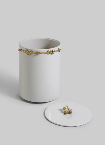 The VIYA Saffron Ecru Bin With Lid is a white ceramic cylinder with a gold accent near the top. Its matching lid, featuring a small gold handle, is placed beside it on a light grey background.