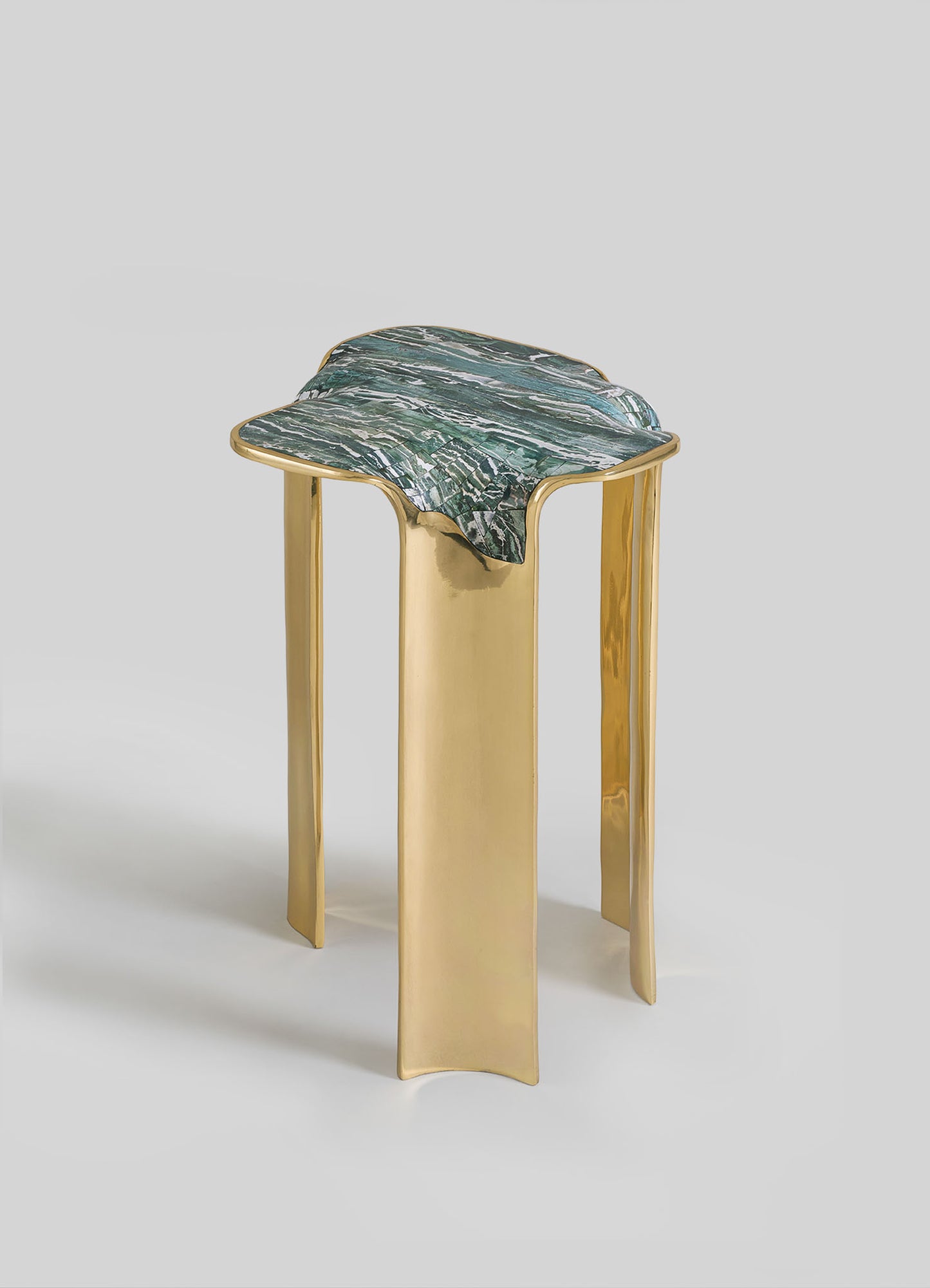 The Coonoor Side Table by VIYA features sculpted gold legs inspired by cast brass jewelry and a uniquely wavy green marble top reminiscent of Indian landscapes, shown against a plain light gray background.