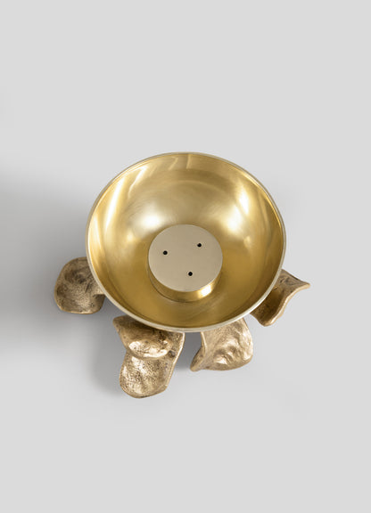 The Glory Lily Incense Diya by VIYA, a gold metal bowl with a smooth finish, sits atop an abstract base crafted from four textured, gold elements—an elegant piece photographed from above on a plain light gray background that evokes the artistry of ancient metalworking techniques.
