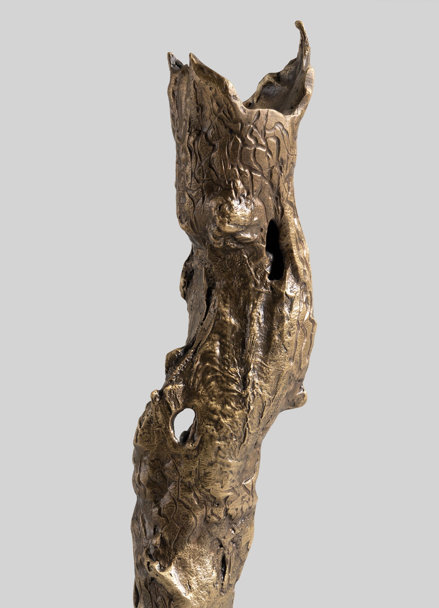 The VIYA Kikar Candle Holder Large features a bronze finish with a weathered, textured tree trunk design and hollow sections, inspired by metalworking traditions, set against a plain light gray background.