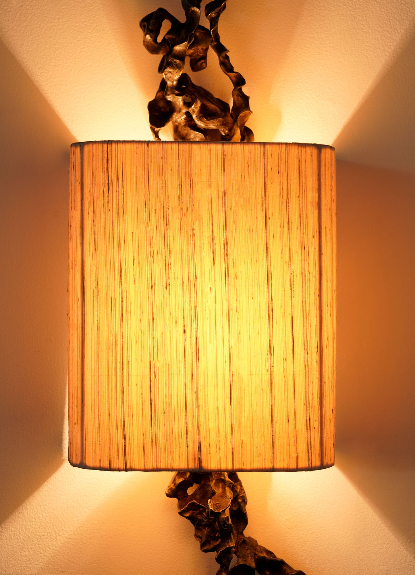The VIYA Andaman Wall Sconce B features a cylindrical, textured shade that emits warm light with symmetrical patterns. Brass accents echo organic forms, inspired by the intricate caves of the Andaman Islands.