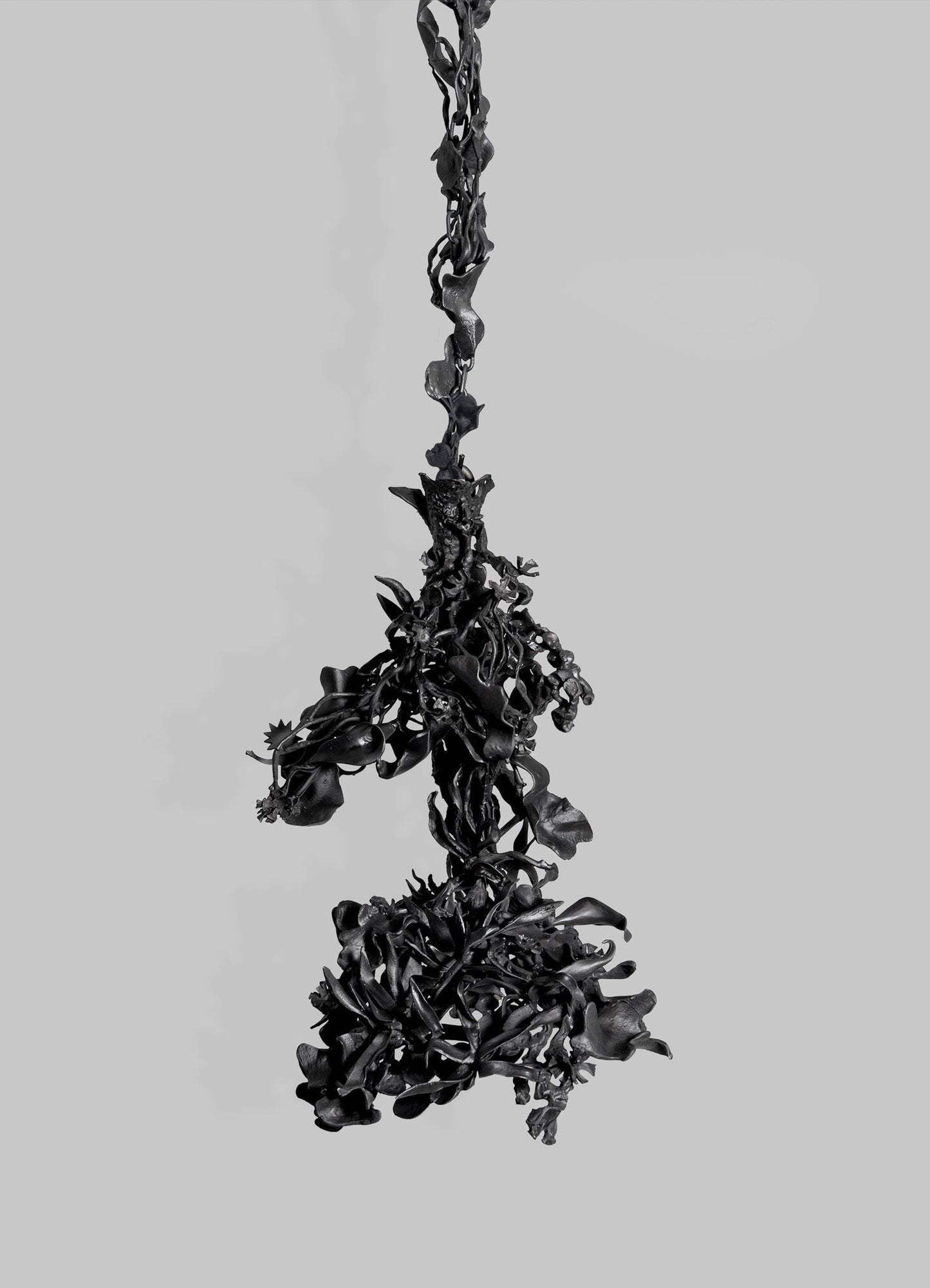 The Gardens Of India Pendant Light by VIYA features dark, twisted organic forms suspended on a plain gray backdrop, evoking abstract plant matter and echoing the cultural symbolism of Indian gardens in its intricate design.