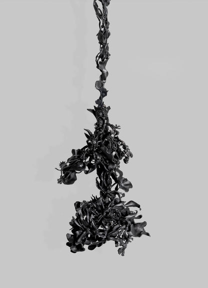 The Gardens Of India Pendant Light by VIYA features dark, twisted organic forms suspended on a plain gray backdrop, evoking abstract plant matter and echoing the cultural symbolism of Indian gardens in its intricate design.