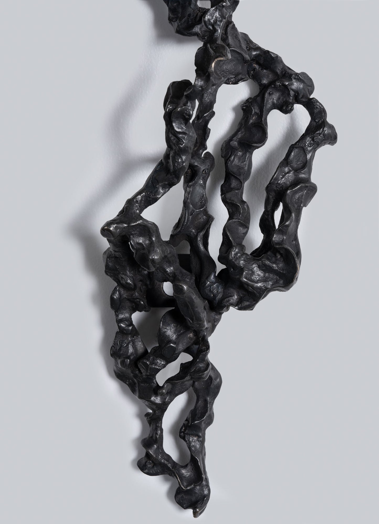The Andaman Wall Sconce B by VIYA features a black, twisted, organic sculptural form with a rough, wavy texture that casts subtle shadows on a light gray background.