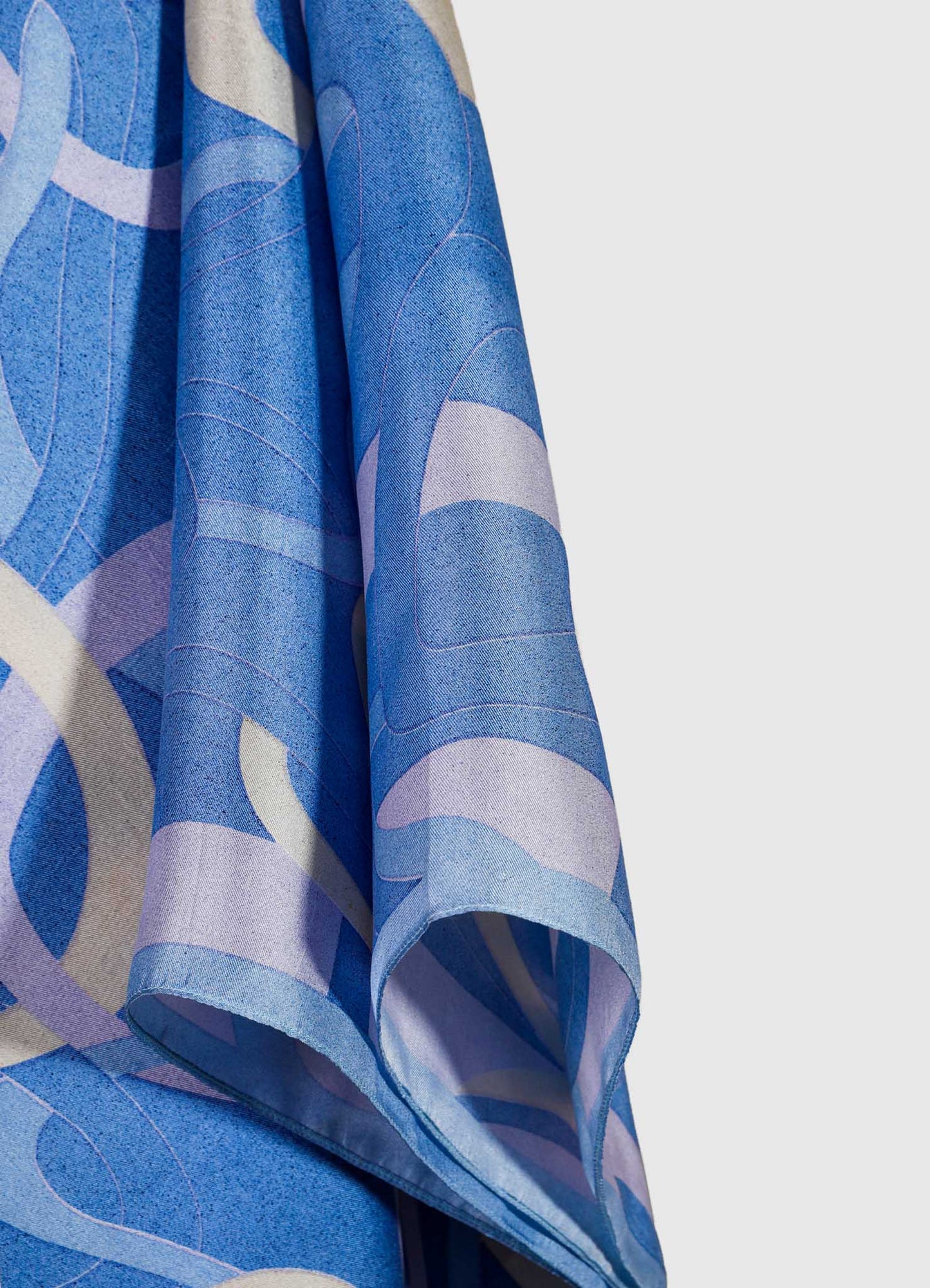 A close-up of a fabric curtain with an abstract geometric pattern in shades of blue and light purple. The material appears to be lightweight with a soft drape, emphasizing a modern or contemporary style.