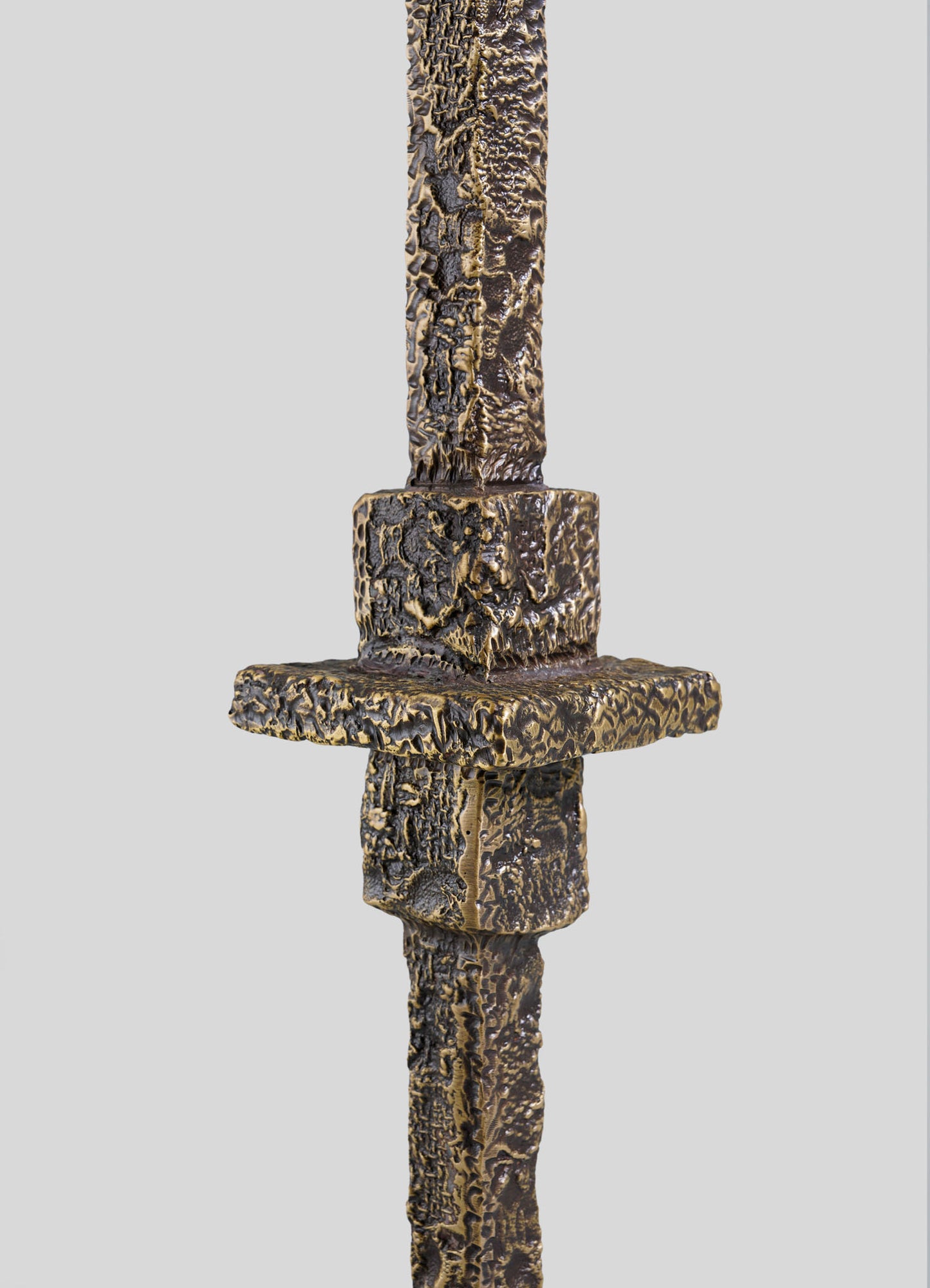 Close-up of the Tiruppur Totem Candle Holder Large by VIYA, showcasing its textured, weathered bronze-like surface with intricate brocade patterns, set against a plain light gray background.