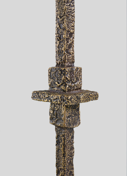 Close-up of the Tiruppur Totem Candle Holder Large by VIYA, showcasing its textured, weathered bronze-like surface with intricate brocade patterns, set against a plain light gray background.