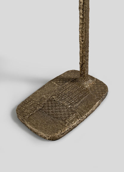 The VIYA Mosaic Red Side Table, featuring a textured rectangular metallic base with a vertical rod attached at one end, is displayed against a plain gray background.