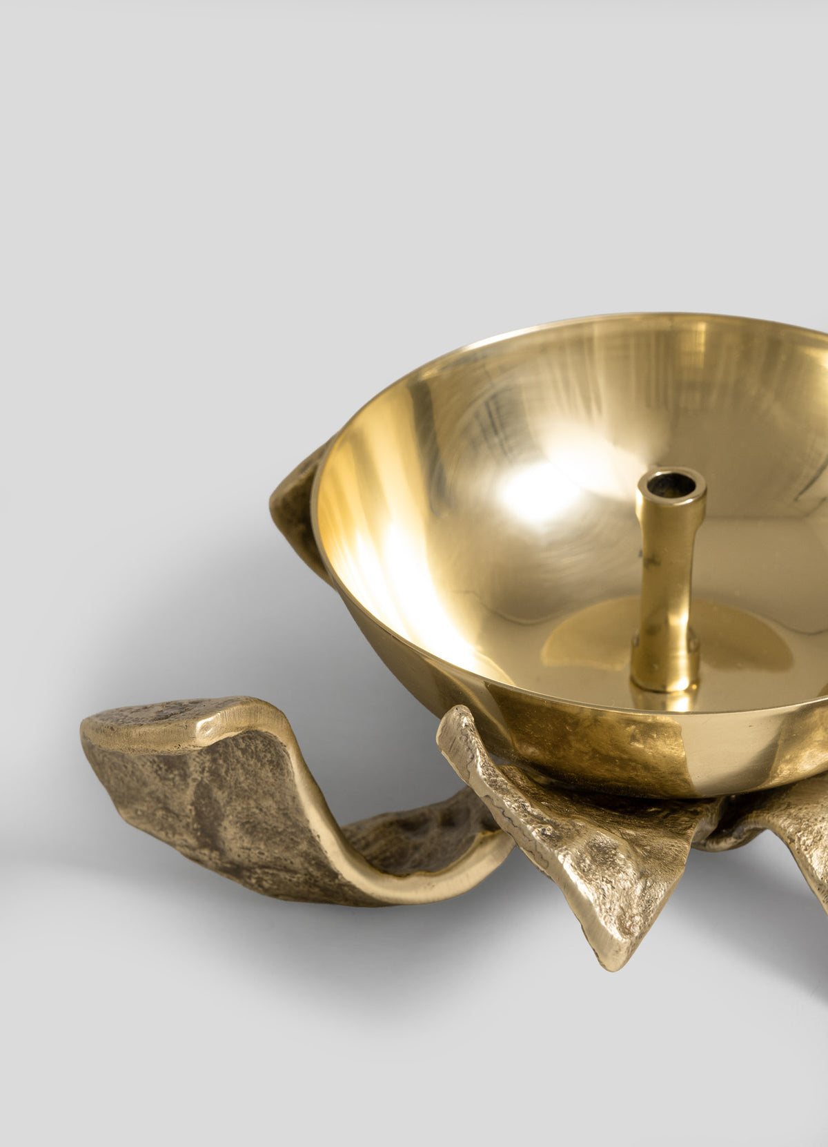 A close-up of the VIYA Glory Lily Eternal Diya—a gold metal bowl with a central spout, supported by three abstract, textured metal legs and expertly crafted using ancient metalworking techniques—set against a plain light gray background.