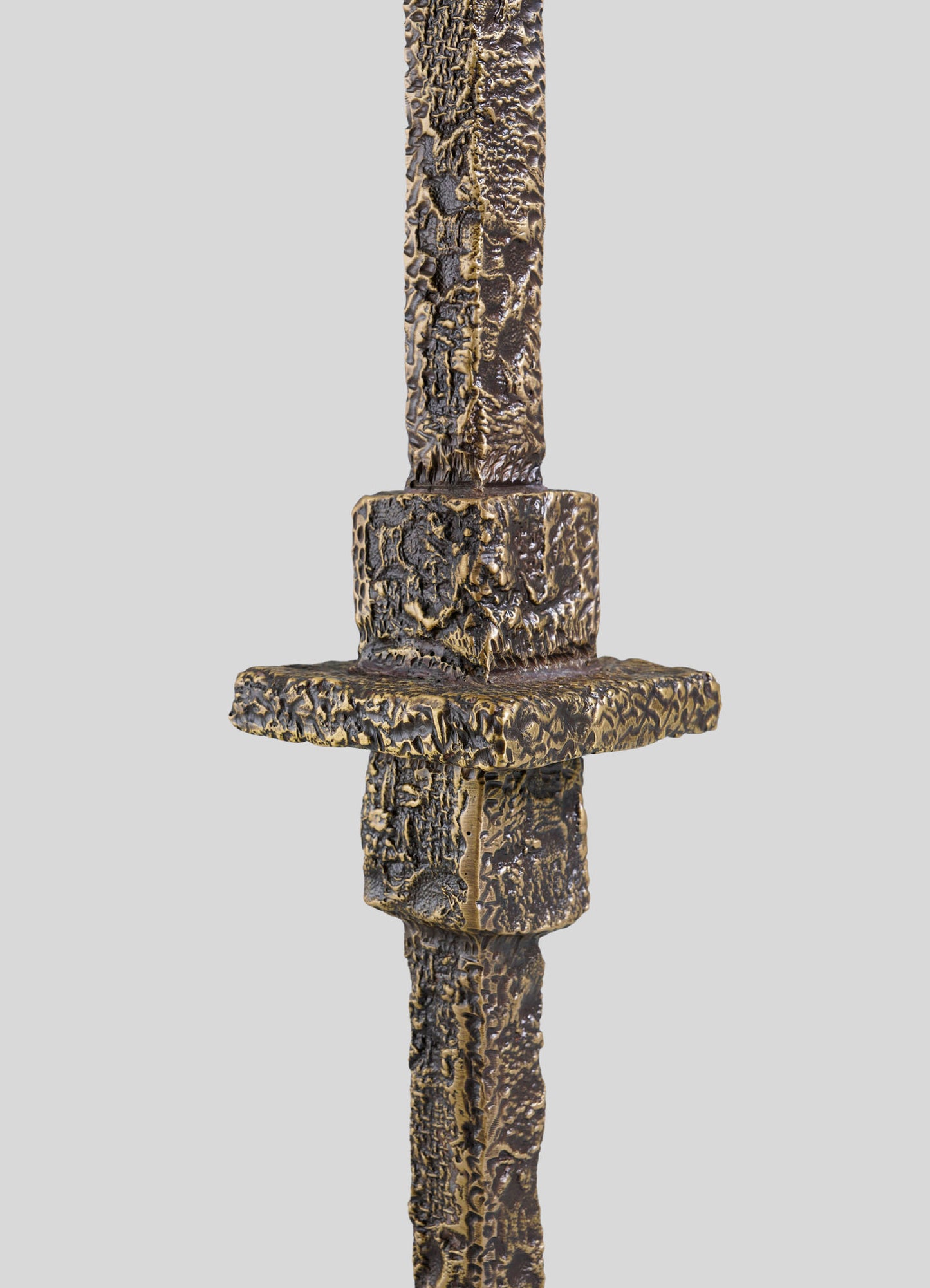 Close-up of the VIYA Tiruppur Totem Candle Holder Small, featuring a textured bronze finish and a central square cross-like design inspired by Indian brocades, set against a plain gray background.