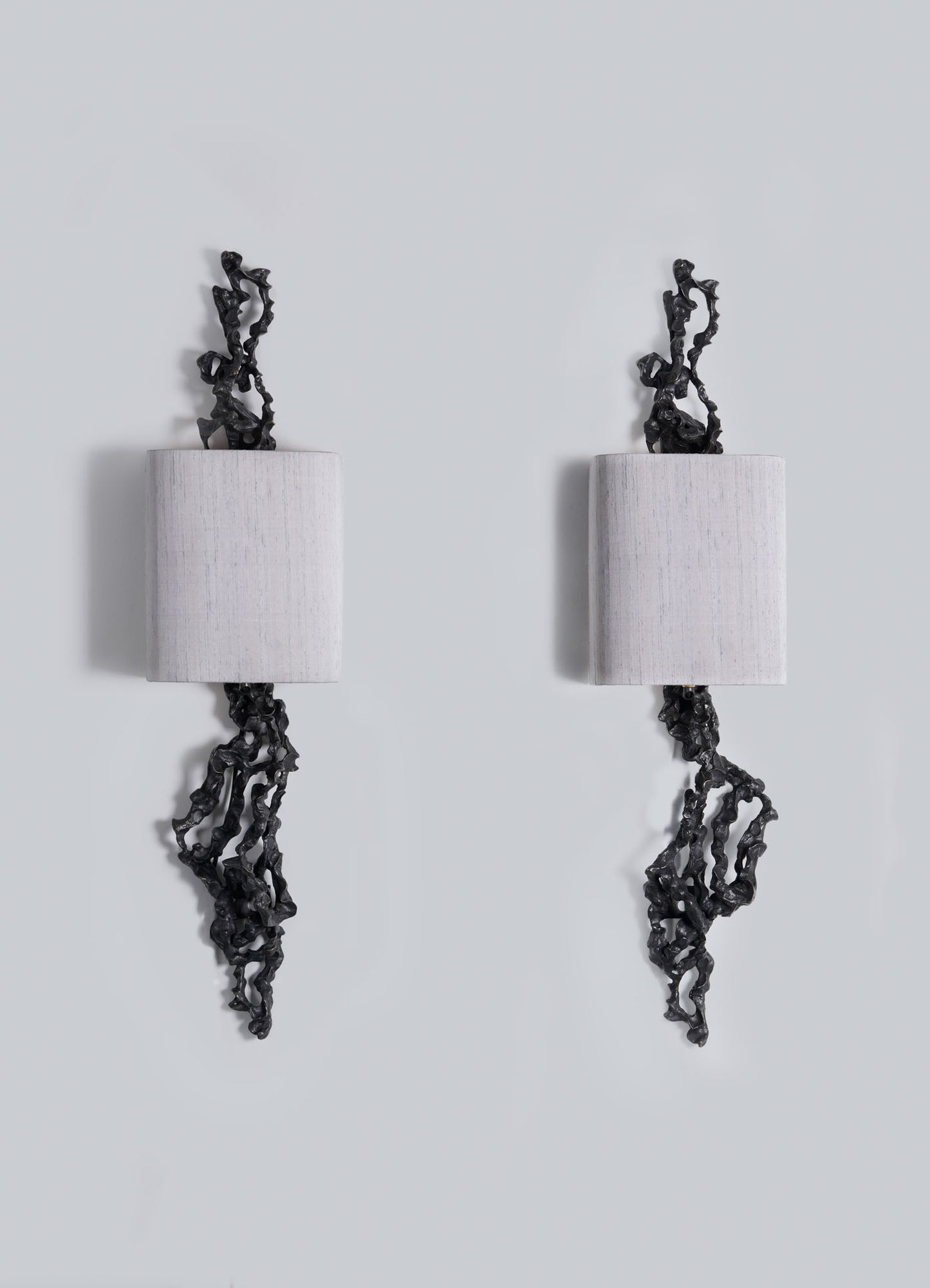 Two rectangular Andaman Wall Sconce A lamps by VIYA are mounted on a light gray wall, each featuring black organic forms that twist from their edges in a mirrored, abstract design inspired by sculptural elements of the Andaman Islands.