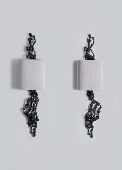 Two rectangular Andaman Wall Sconce A lamps by VIYA are mounted on a light gray wall, each featuring black organic forms that twist from their edges in a mirrored, abstract design inspired by sculptural elements of the Andaman Islands.