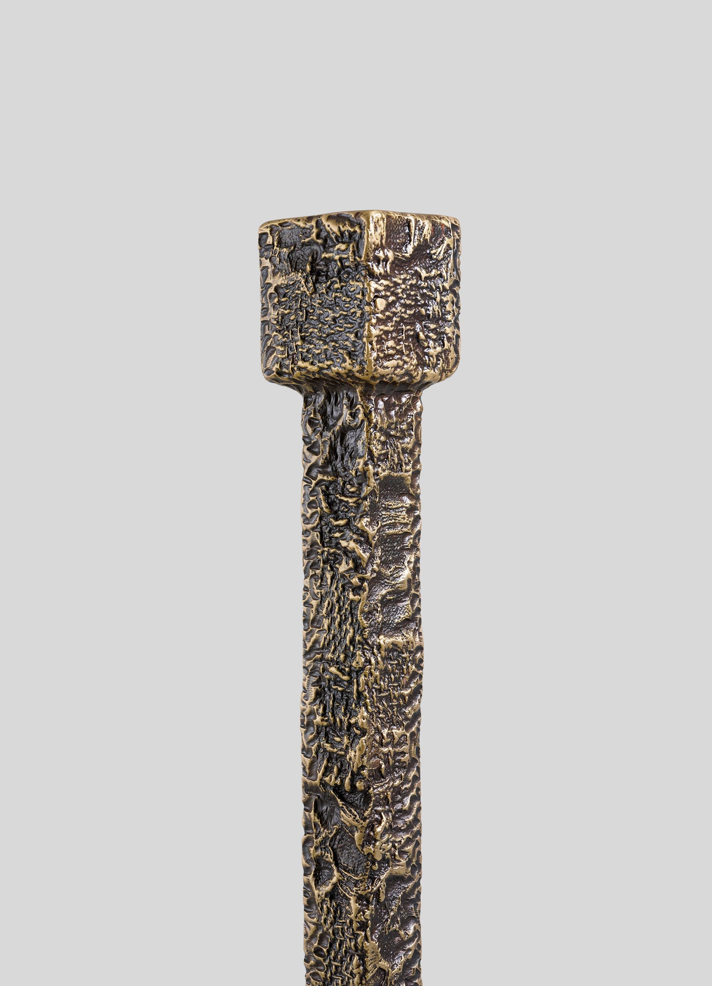 A close-up of the VIYA Tiruppur Totem Candle Holder Large, featuring a textured, metallic finish with a square top and cylindrical body reminiscent of handwoven fabrics, set against a plain light gray background.