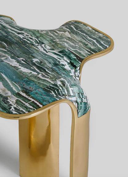 A close-up of the VIYA Coonoor Side Table, featuring a wavy abstract green and white top inspired by Indian landscapes and smooth gold metal legs, set against a plain light gray background.
