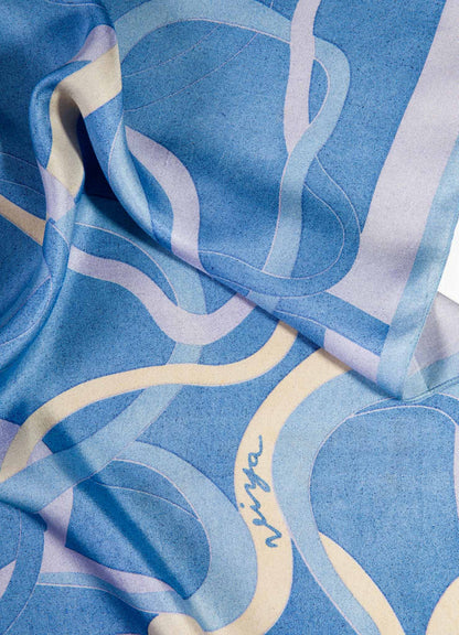 Printed silk scarf with abstract blue and white line motifs and handwritten text, featuring a smooth, lightweight texture.