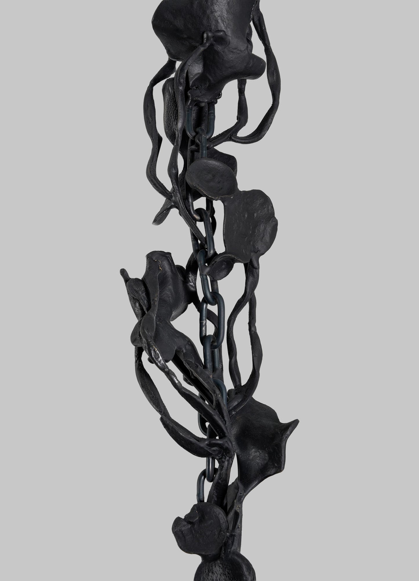 Close-up of the VIYA Gardens Of India Pendant Light—a dark metal chain entwined with sculpted, abstract floral and vine motifs—evoking fragrant blossoms, set against a plain gray background.