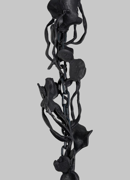 Close-up of the VIYA Gardens Of India Pendant Light—a dark metal chain entwined with sculpted, abstract floral and vine motifs—evoking fragrant blossoms, set against a plain gray background.