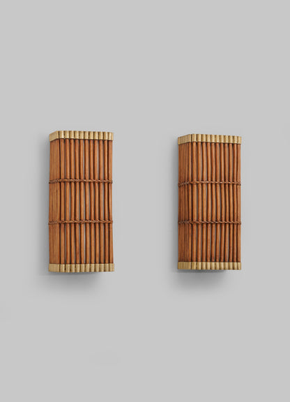 Two Namsai Wall Sconces by VIYA, crafted from vertical bamboo rods and framed in light-colored wood, are mounted on a plain gray wall, exemplifying the charm of handcrafted lighting inspired by traditional Indian techniques.