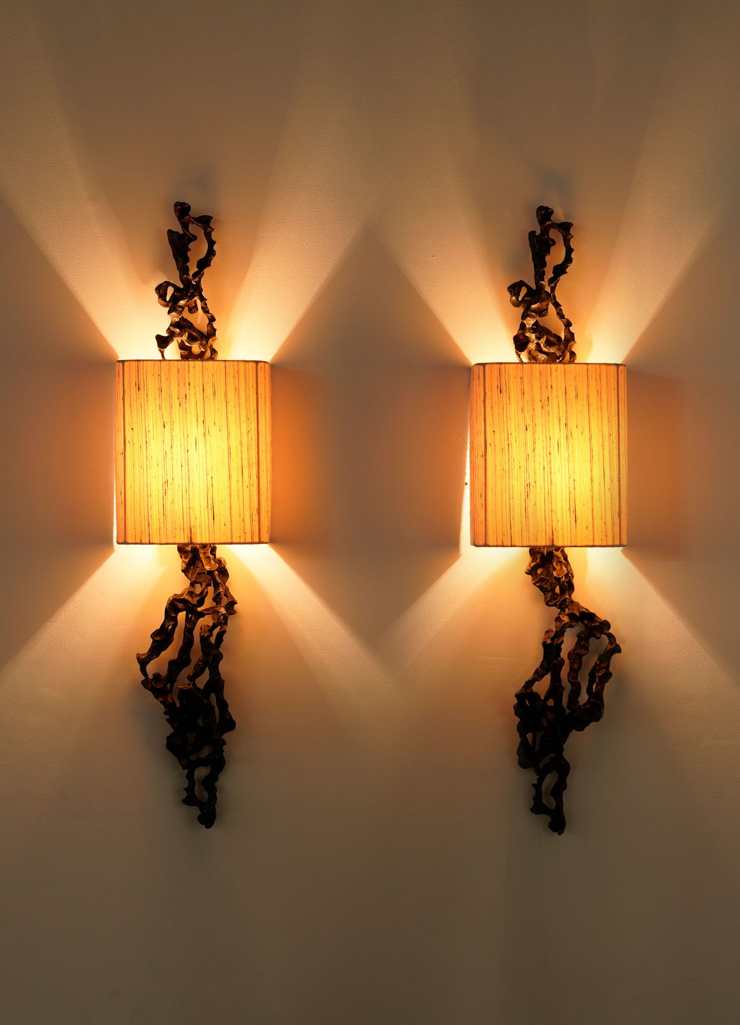 The VIYA Andaman Wall Sconce B features a modern, dark twisted metal design inspired by Andaman Islands caves and a rectangular beige lampshade, emitting warm, soft light that creates an inviting ambiance on your wall.