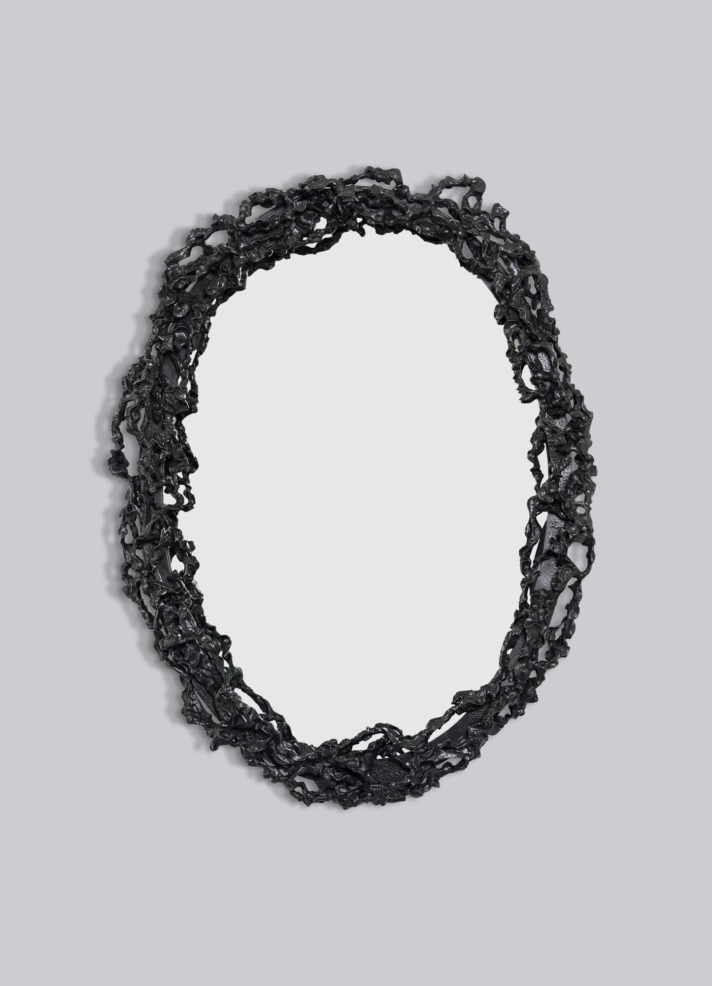 The VIYA Andaman Mirror Large features an oval shape with a textured, irregular black frame inspired by organic forms, like twisted branches or vines, set against a plain light gray background.