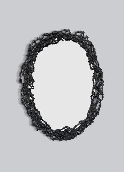 The VIYA Andaman Mirror Large features an oval shape with a textured, irregular black frame inspired by organic forms, like twisted branches or vines, set against a plain light gray background.