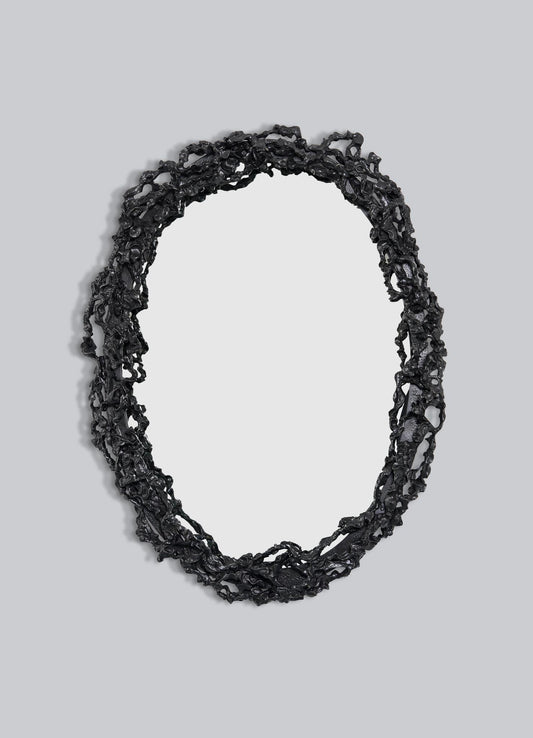 The VIYA Andaman Mirror Large features an oval shape with a textured, irregular black frame inspired by organic forms, like twisted branches or vines, set against a plain light gray background.