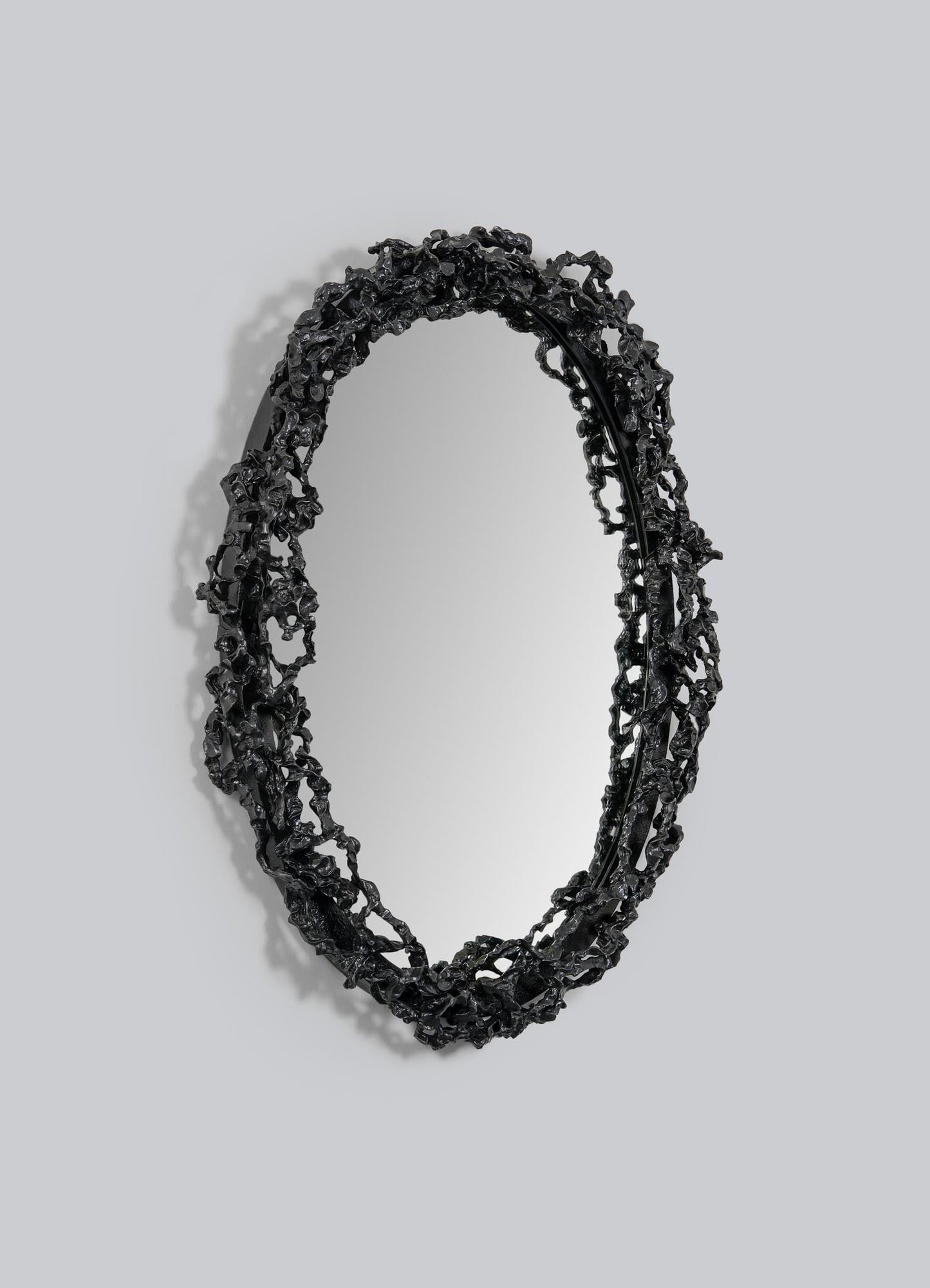 The Andaman Mirror Large by VIYA features an oval shape and a textured black frame inspired by the natural forms of the Andaman Islands caves, shown here mounted on a plain light gray wall.