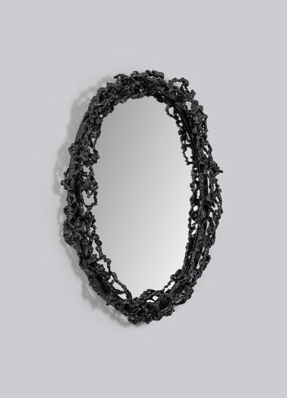 The Andaman Mirror Large by VIYA features an oval shape and a textured black frame inspired by the natural forms of the Andaman Islands caves, shown here mounted on a plain light gray wall.