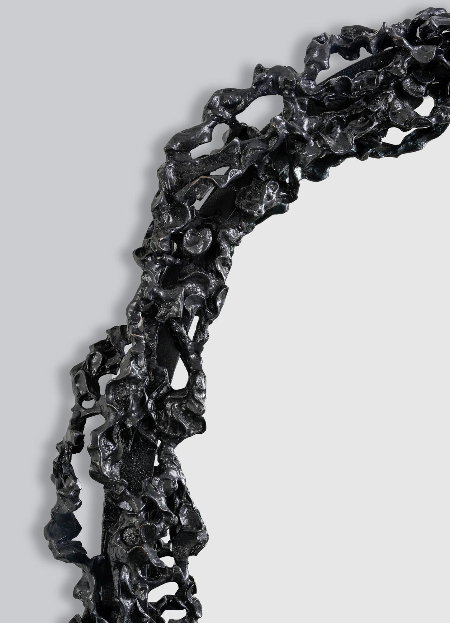 Close-up of the Andaman Mirror Large by VIYA—a black sculptural frame with an irregular, organic texture resembling twisted metal—curving and partially enclosing a blank white space against a plain gray background.
