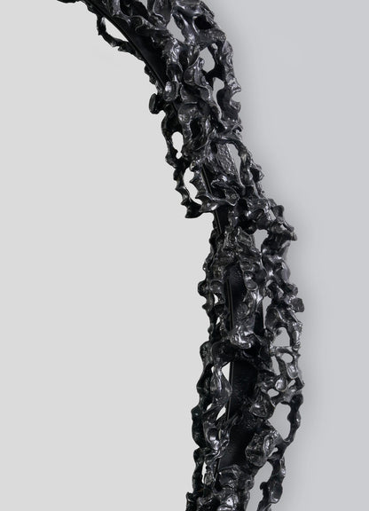 A close-up of the Andaman Mirror Large by VIYA, featuring a sculptural, textured black frame with irregular, cave-inspired forms, set against a plain light gray background.