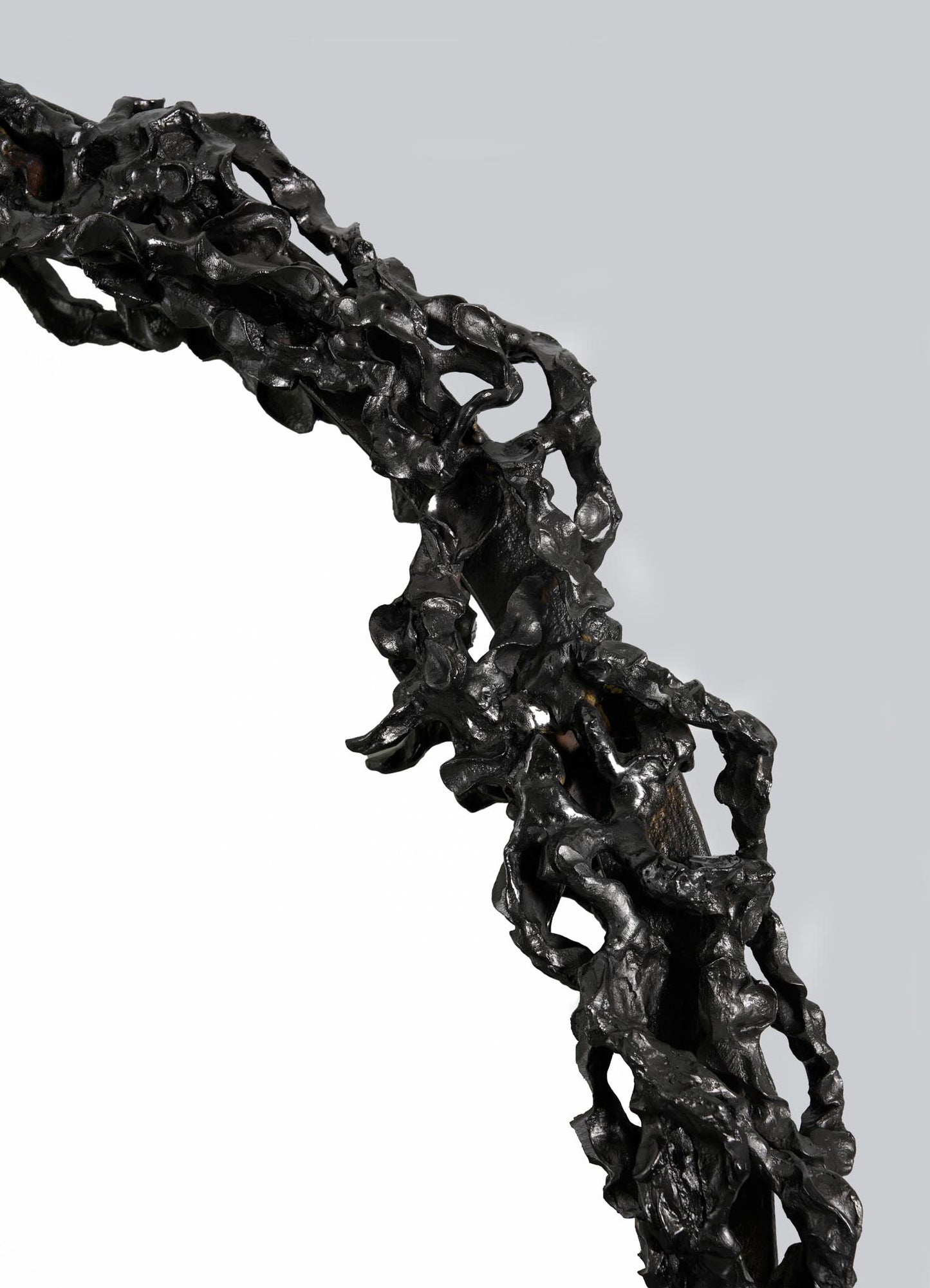 Close-up of the Andaman Mirror by VIYA, featuring an irregular, abstract black frame with organic forms and a rough, sculpted texture reminiscent of twisted metal, set against a plain gray background.