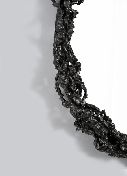 Close-up of the VIYA Andaman Mirror’s ornate round black frame, featuring an abstract, twisted, textured design inspired by organic forms, set against a plain light gray background.