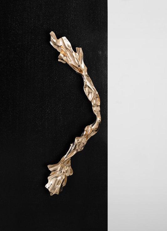 The Aravali Handle A by VIYA, with its sculptural wavy gold form, stands out on a matte black door against a white wall—creating contrast as striking as a bronze side table on black Portoro stone in minimal interiors.
