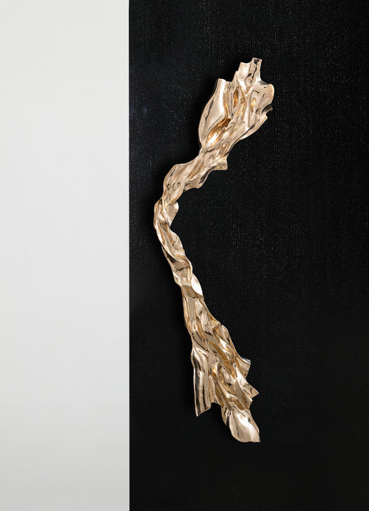 The VIYA Aravali Handle B features a shiny, abstract gold design with flowing, twisted forms, mounted vertically along the edge of a black and white split background.