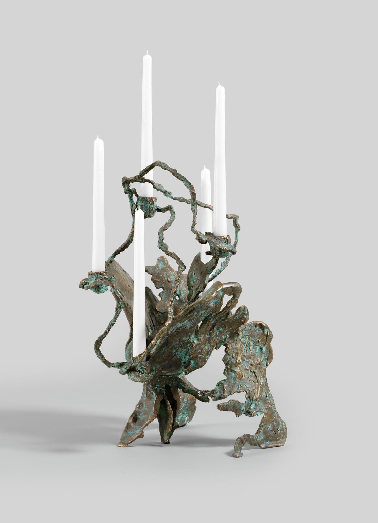 The VIYA Butterfly Candle Stand Large is a sculptural bronze candelabrum with an organic, abstract design, finished in greenish-bronze patina, holding four tall white candles against a plain light gray background.
