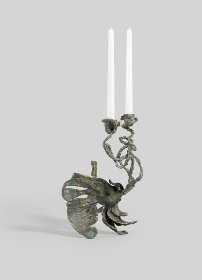 The VIYA Butterfly Candle Stand Medium is a sculptural bronze candelabra with an abstract, organic shape and flowing, textured branches. It holds two white taper candles and is set against a plain gray background.