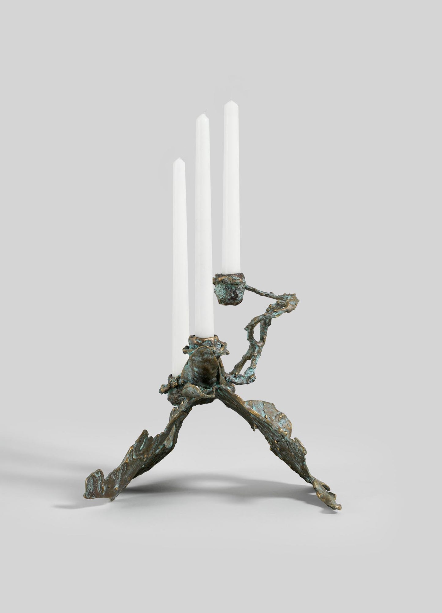 The VIYA Butterfly Candle Stand Small is a sculptural bronze candelabra with an abstract, branch-inspired design, three uneven legs, and holds three white taper candles. Shown on a light gray background.