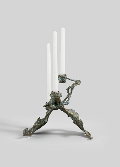 The VIYA Butterfly Candle Stand Small is a sculptural bronze candelabra with an abstract, branch-inspired design, three uneven legs, and holds three white taper candles. Shown on a light gray background.